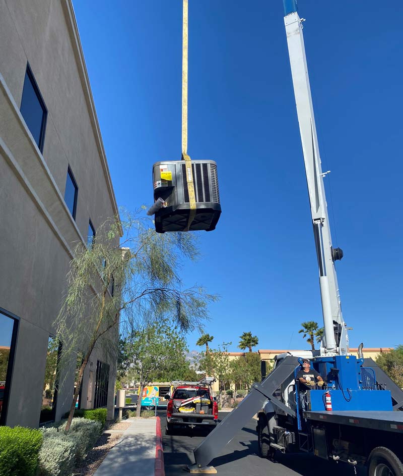 Crane lifting a rooftop AC unit for installation at a commercial site